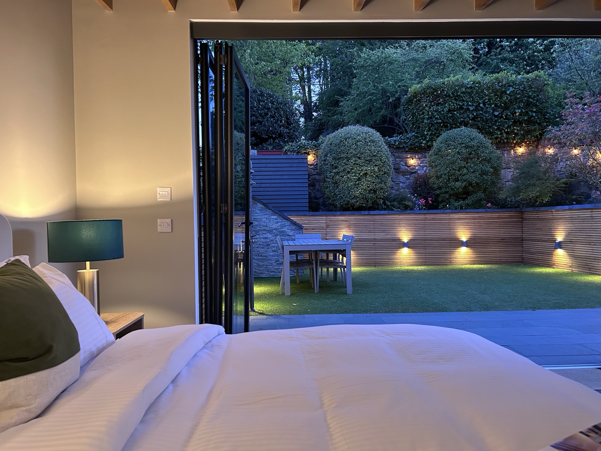 View from the king bed through open bifold doors to the privately lit walled garden at night
