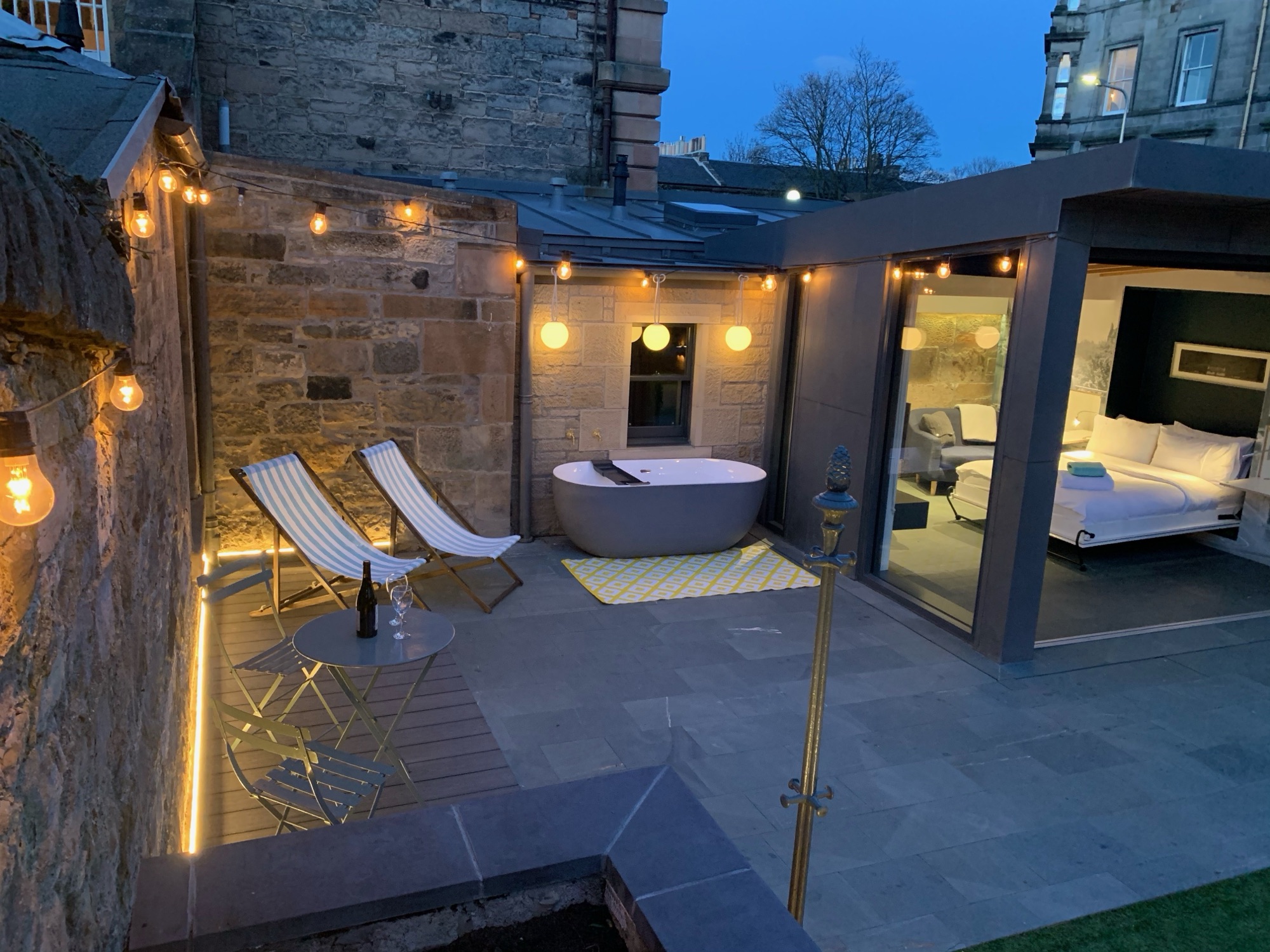 Garden at night with outdoor bath and deckchairs